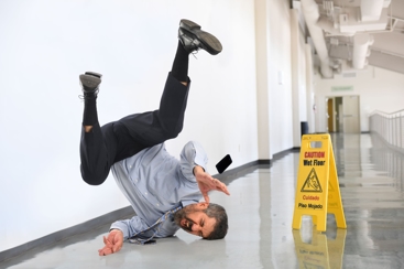 Man slipping and falling on a wet floor, next to a "wet floor" A-frame sign