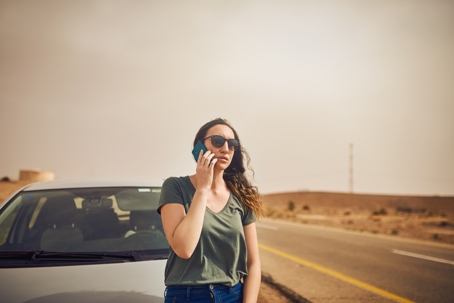Shot of a young woman standing next to her broken down vehicle and using a smartphone after an accident